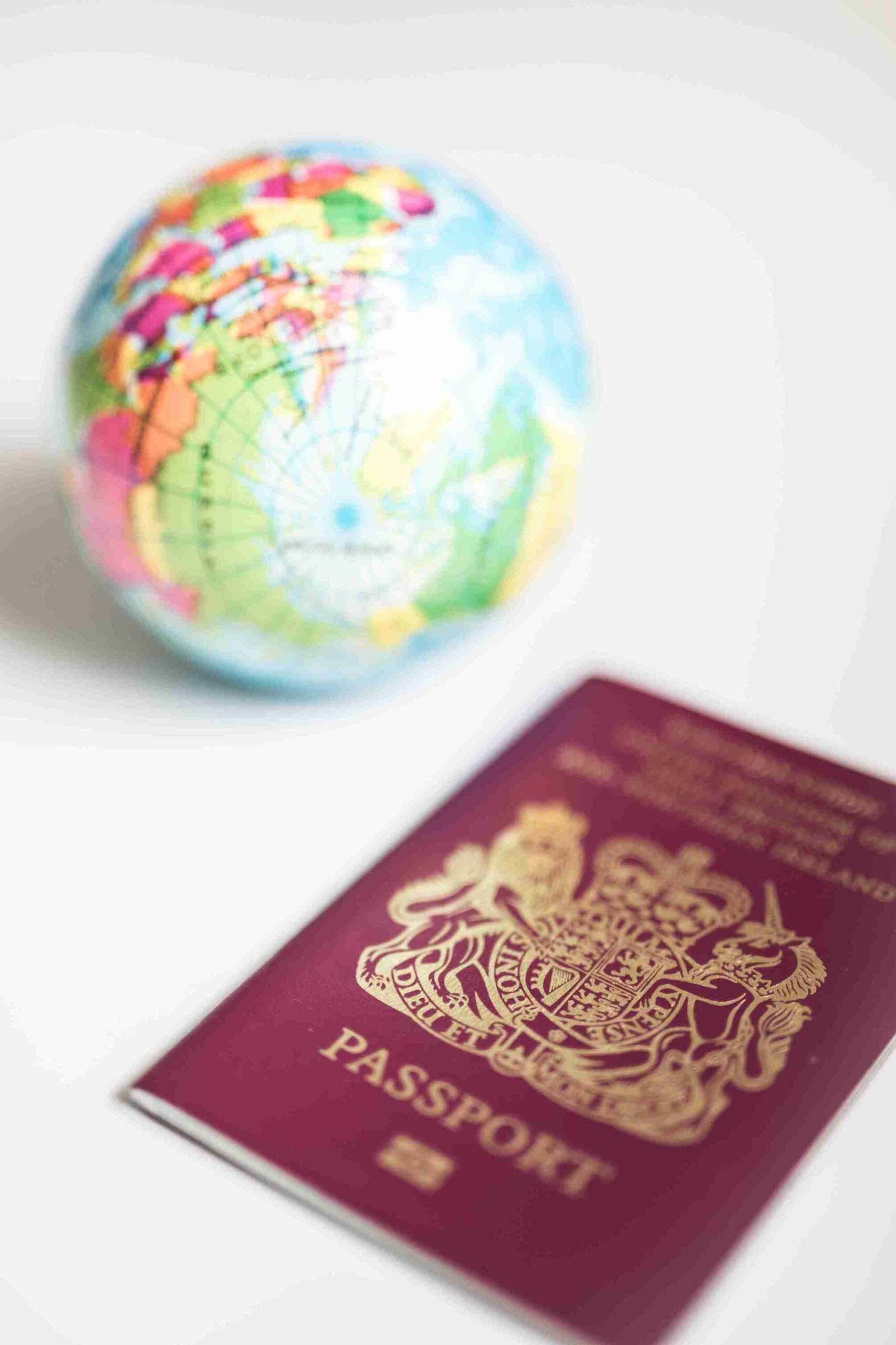 A close-up of a British passport lying on a white surface with a small, colorful globe in the background.