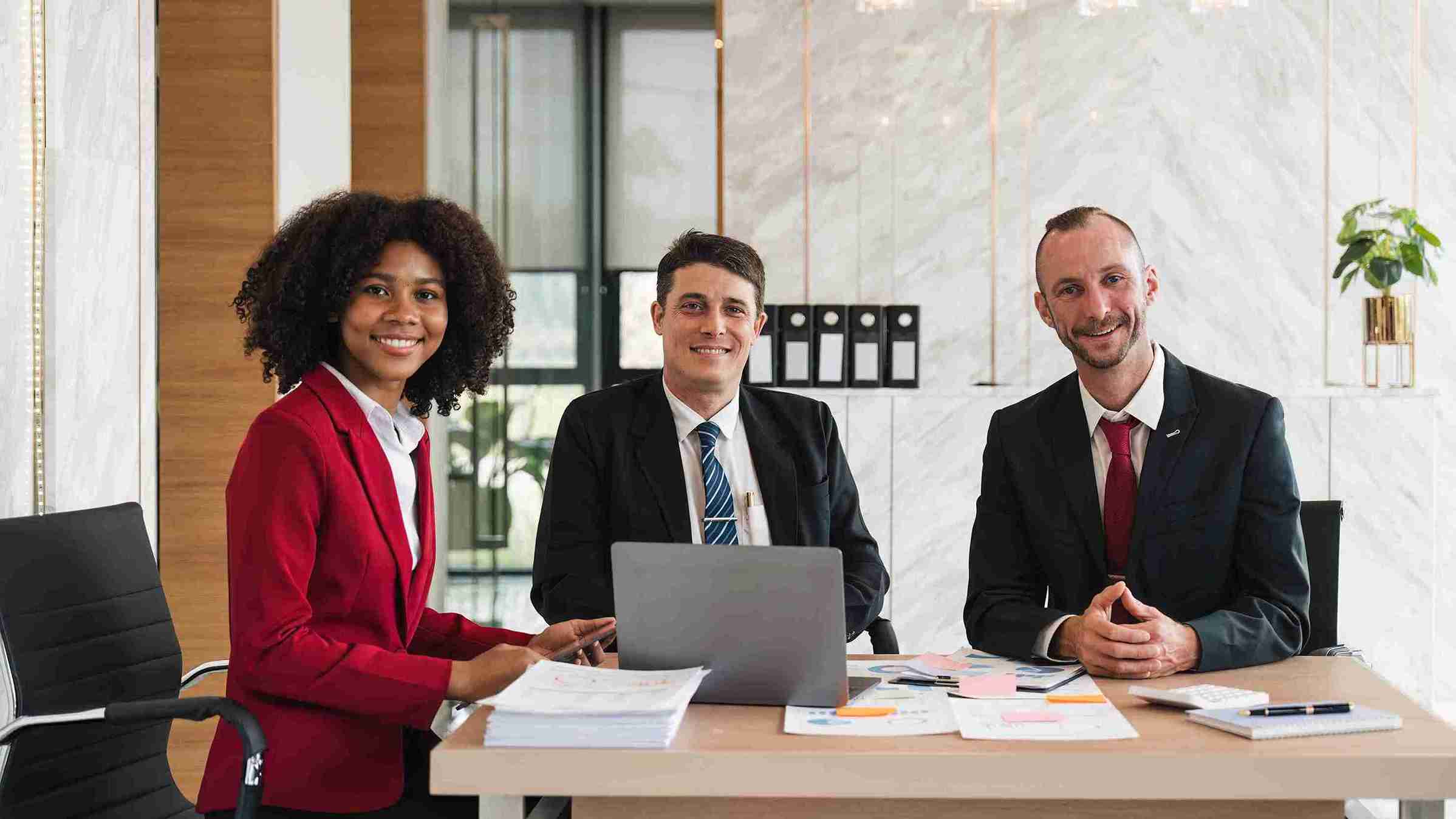 Three business professionals collaborating at a table, each using a laptop for a meeting or discussion.