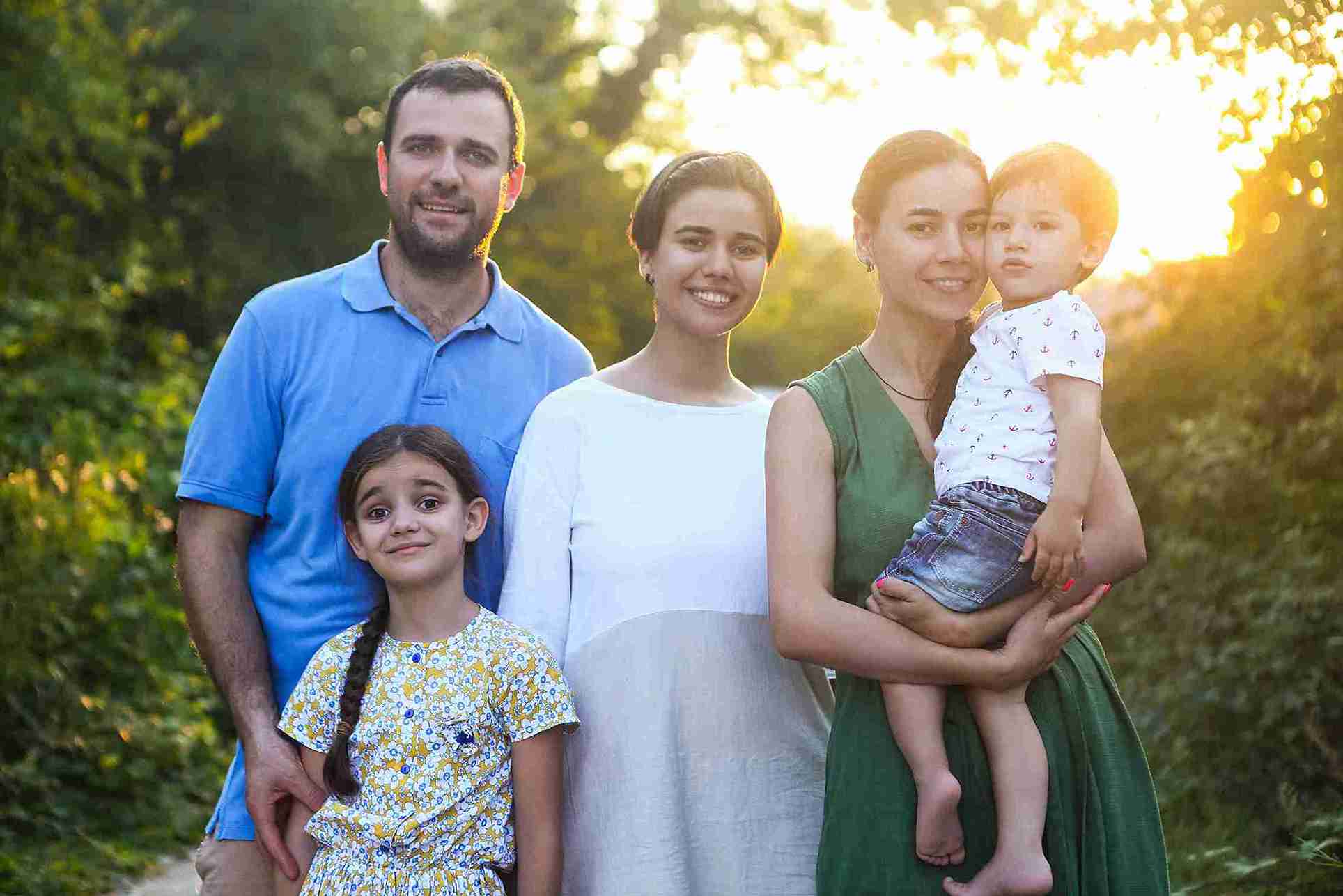 A family smiles together for a sunny outdoor photo, capturing a joyful moment in the warm sunlight.