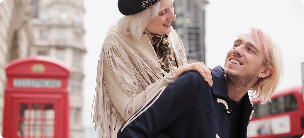 A man and woman smile together in front of a classic red telephone booth.