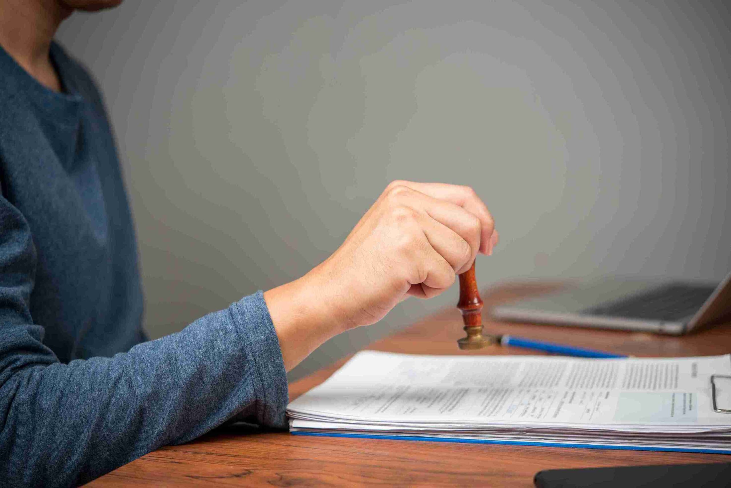 A person stamps a document with a wooden-handled stamp on a desk representing a legally binding Will.