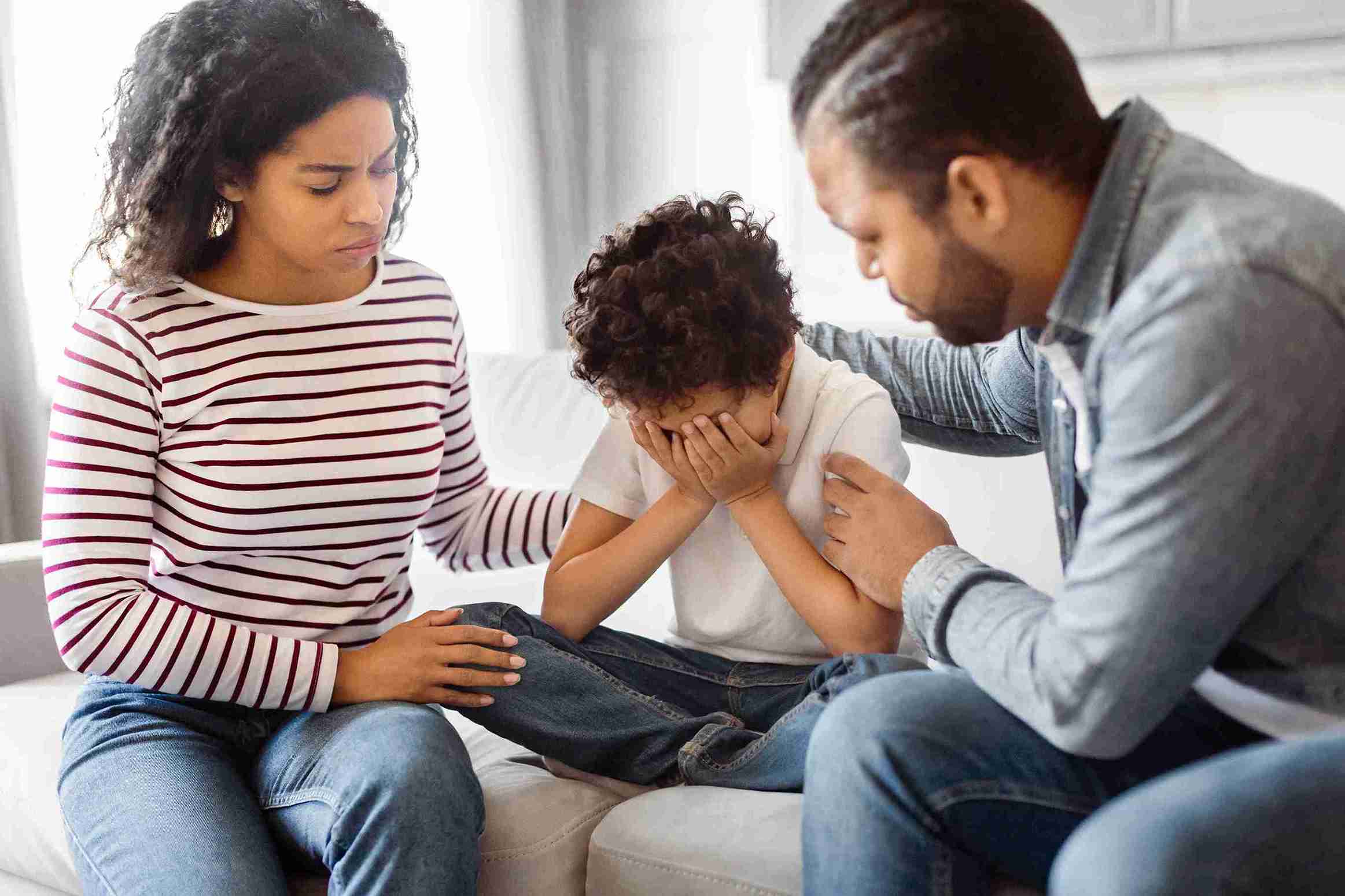 A family sits on a couch, with a child crying in the foreground, conveying a moment of emotional distress.