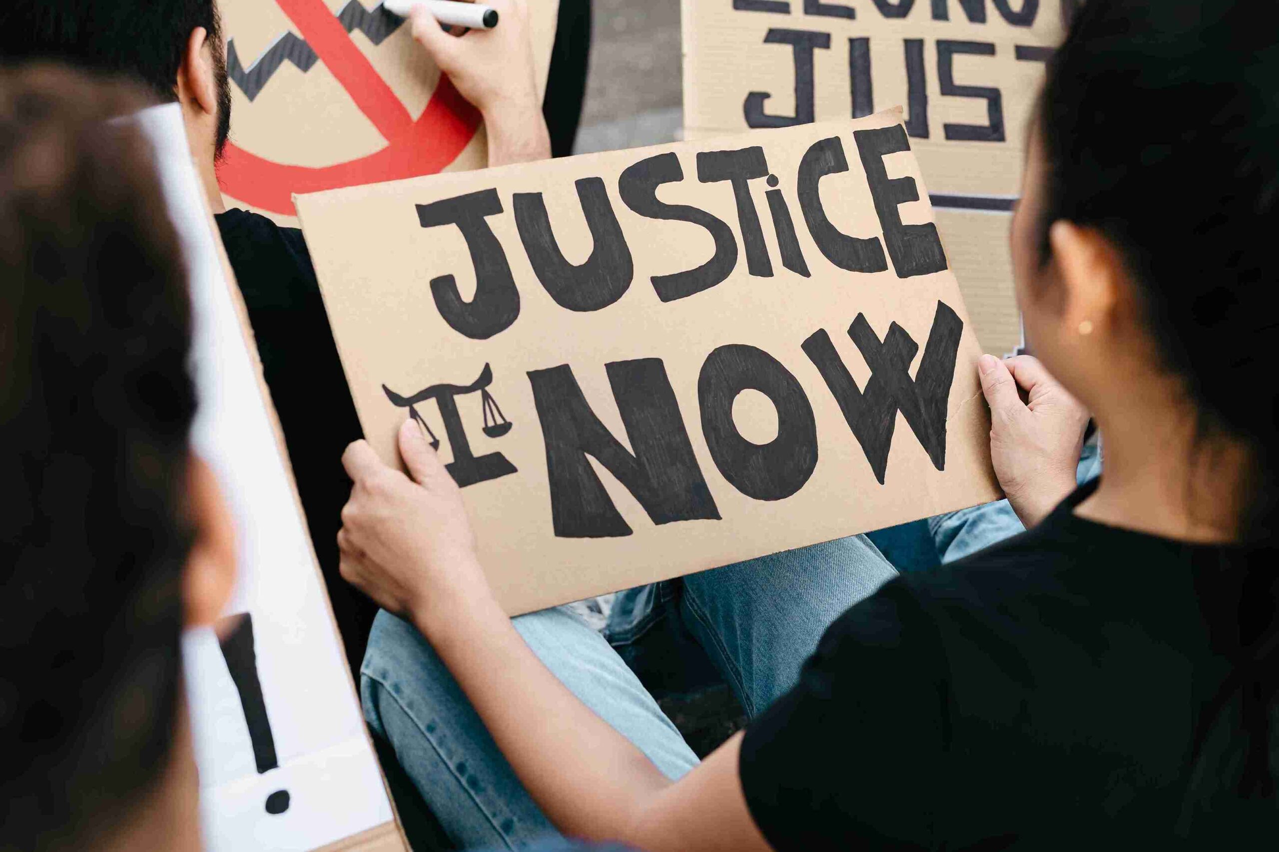 People holding signs that read "Justice Now" during a protest advocating for legal reforms and support for victims.