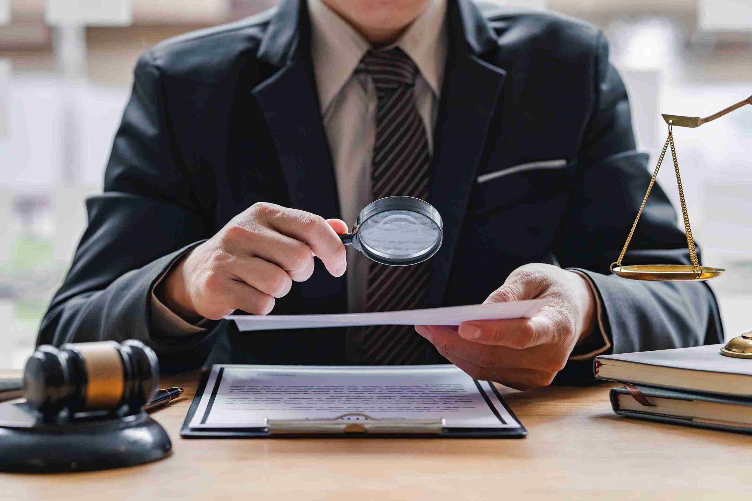 Person in suit examining document with magnifying glass, gavel, and scales, representing VAT inspections and investigations.