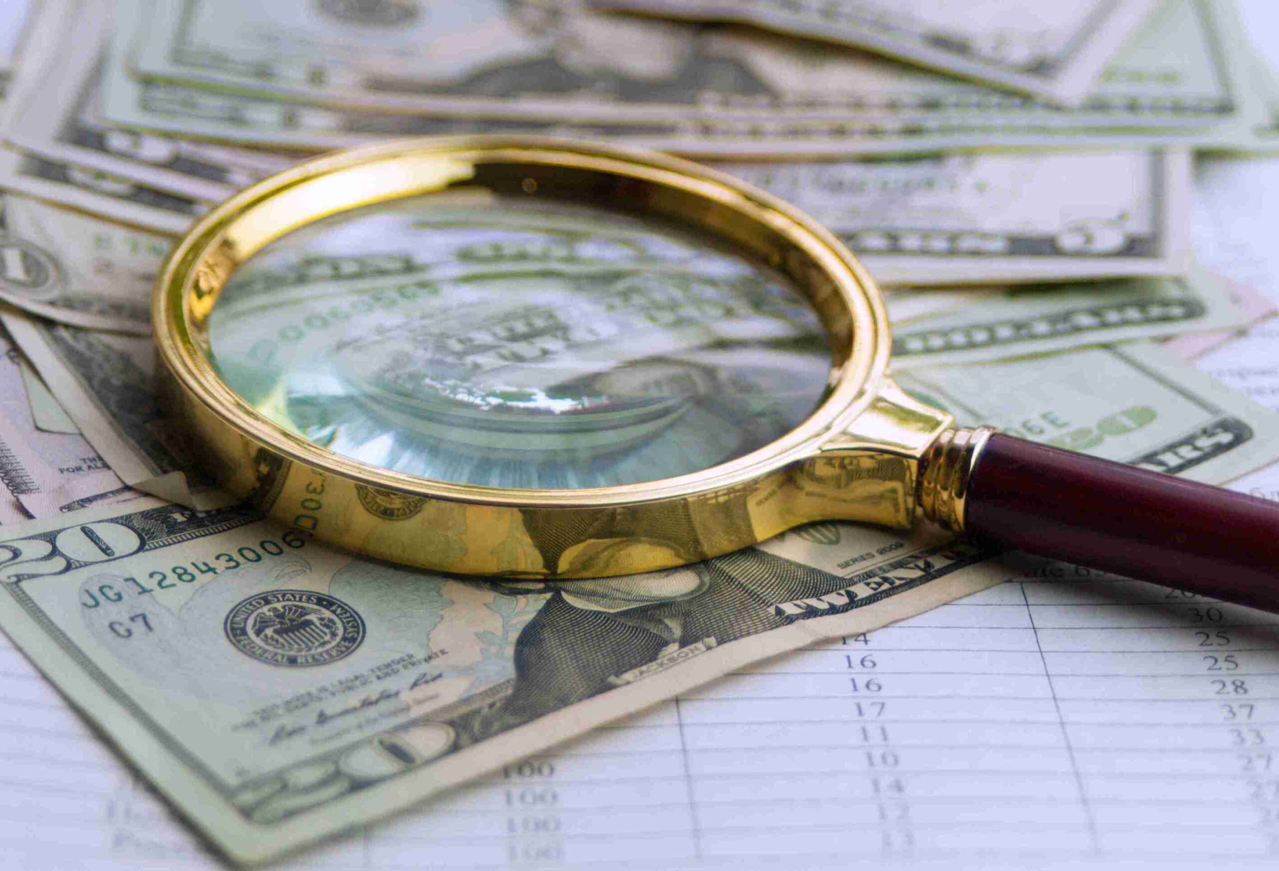 Magnifying glass over currency and spreadsheet, representing PAYE investigations and financial scrutiny.