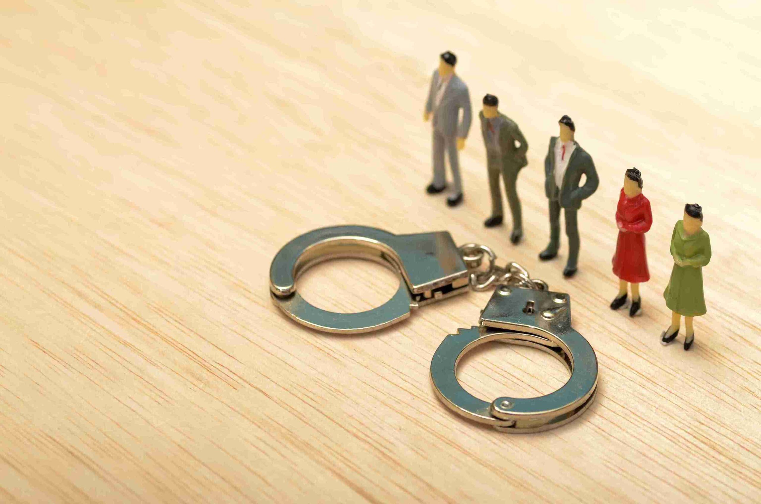 Miniature figures in business suits holding handcuffs, symbolizing authority and restraint in a corporate context.
