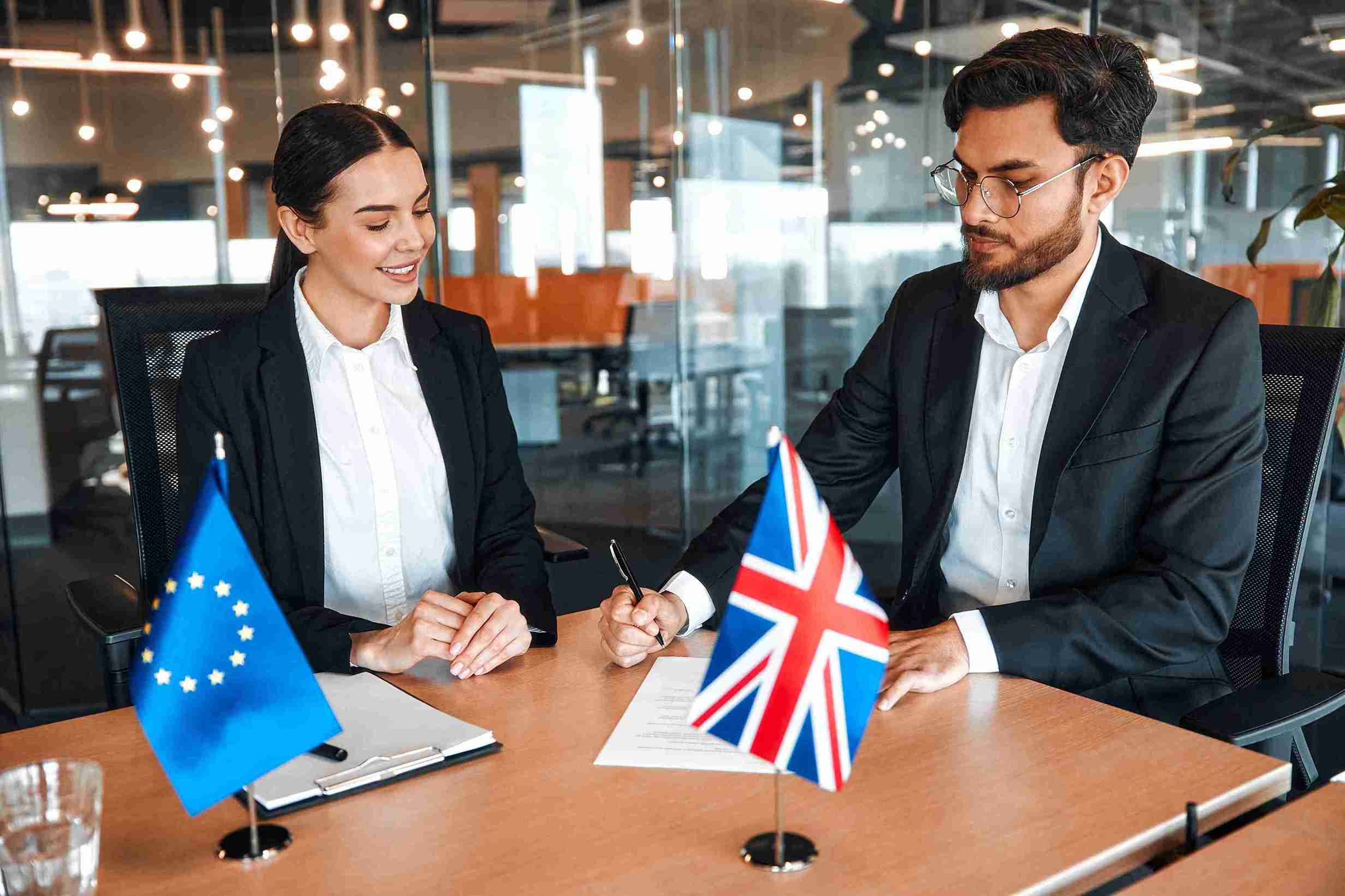 Two business professionals signing a contract at a desk in a modern office setting.