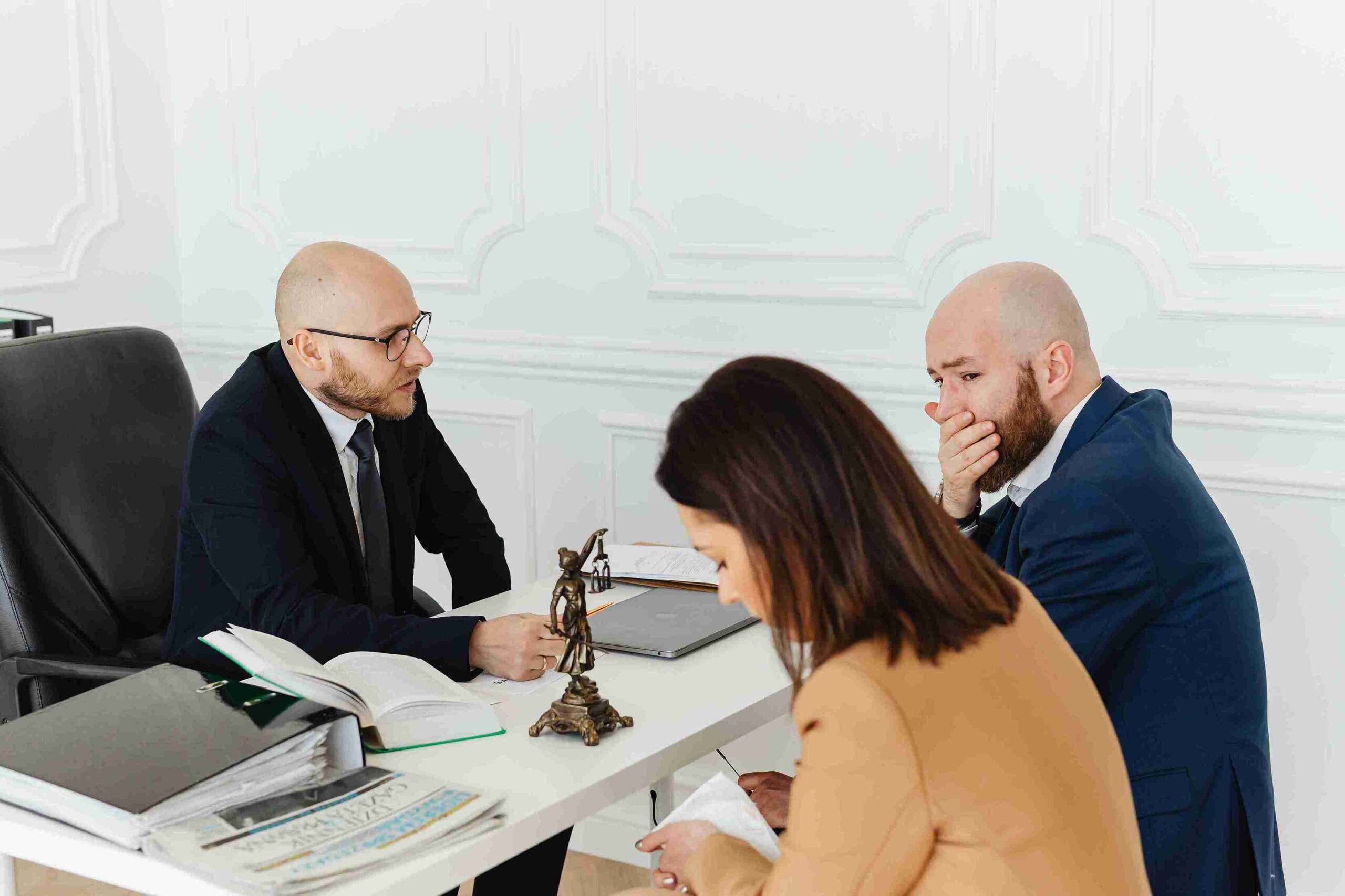 Three people engaged in discussion while sitting at a table in a modern office setting.