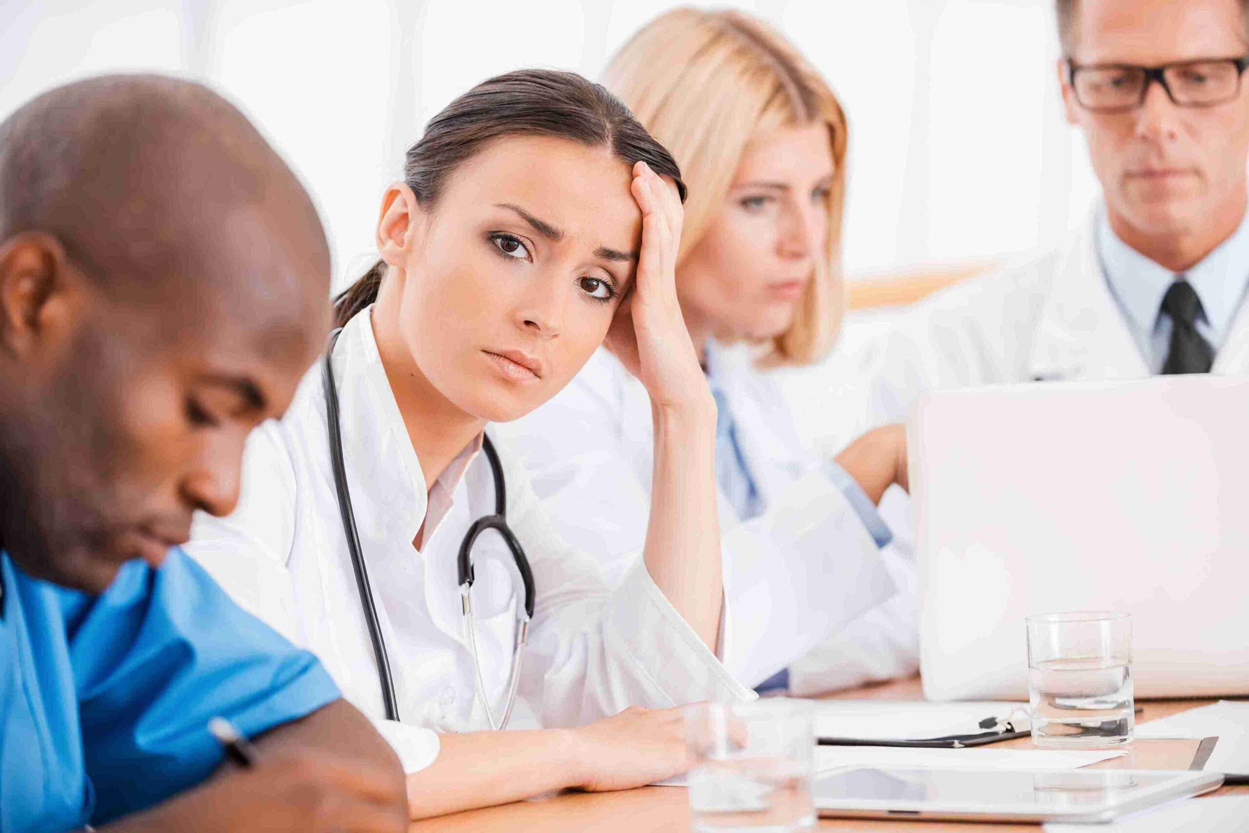 A group of doctors at a table with a laptop, discussing failures to follow proper medical procedures.