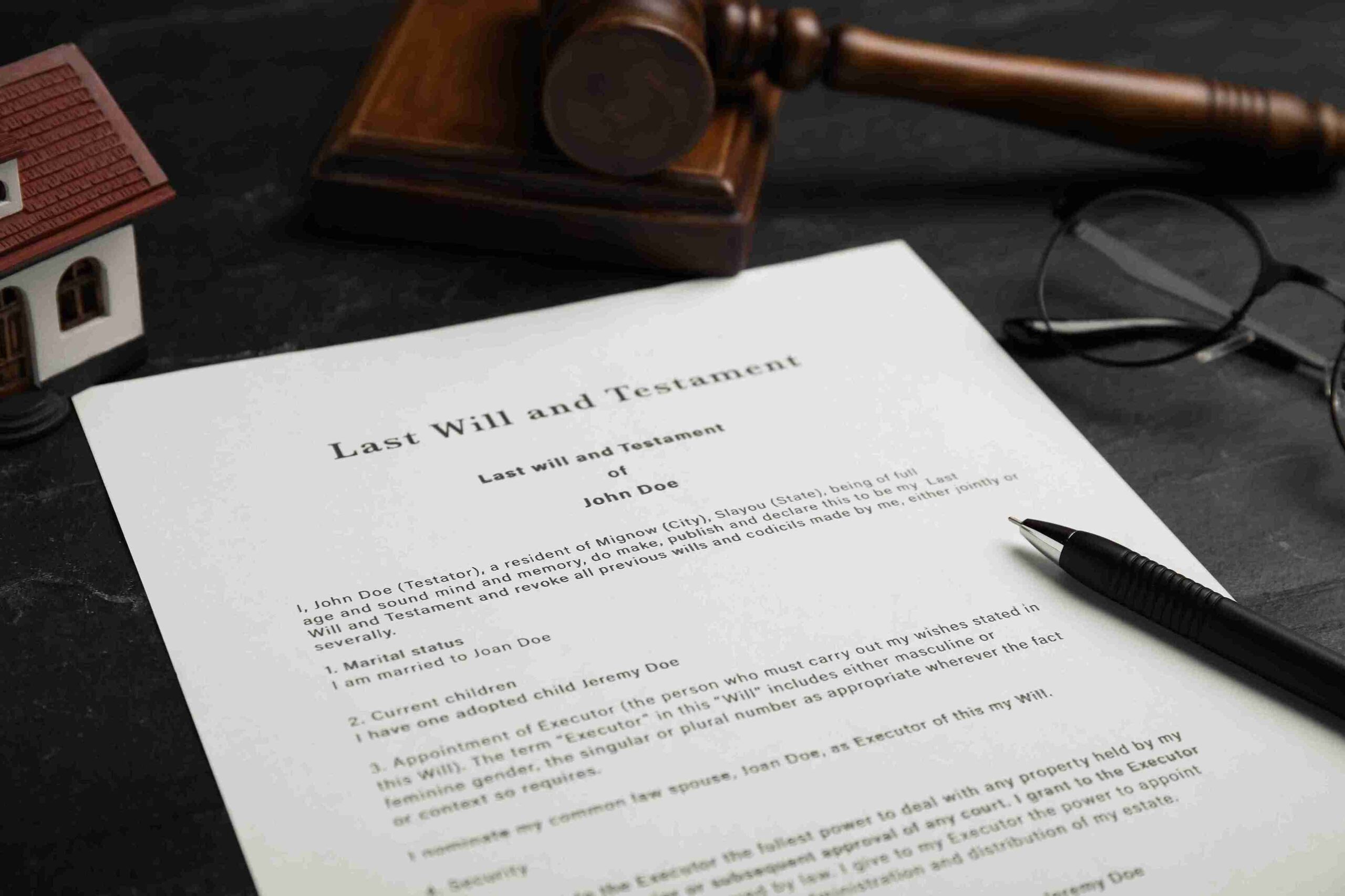 Last Will and Testament on table with gavel, pen, glasses, and model house, representing estate planning.