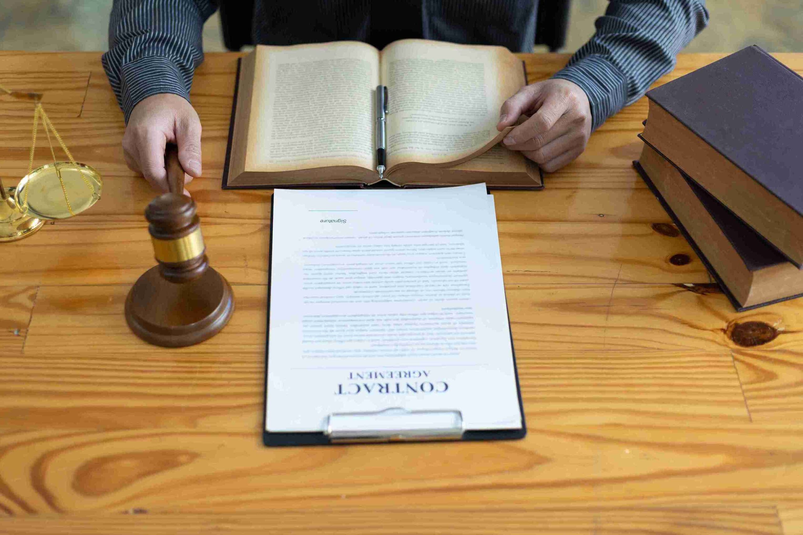 Person reading legal book at desk with gavel and scales, representing the importance of a Lasting Power of Attorney as a safeguard against future legal and financial hardship.