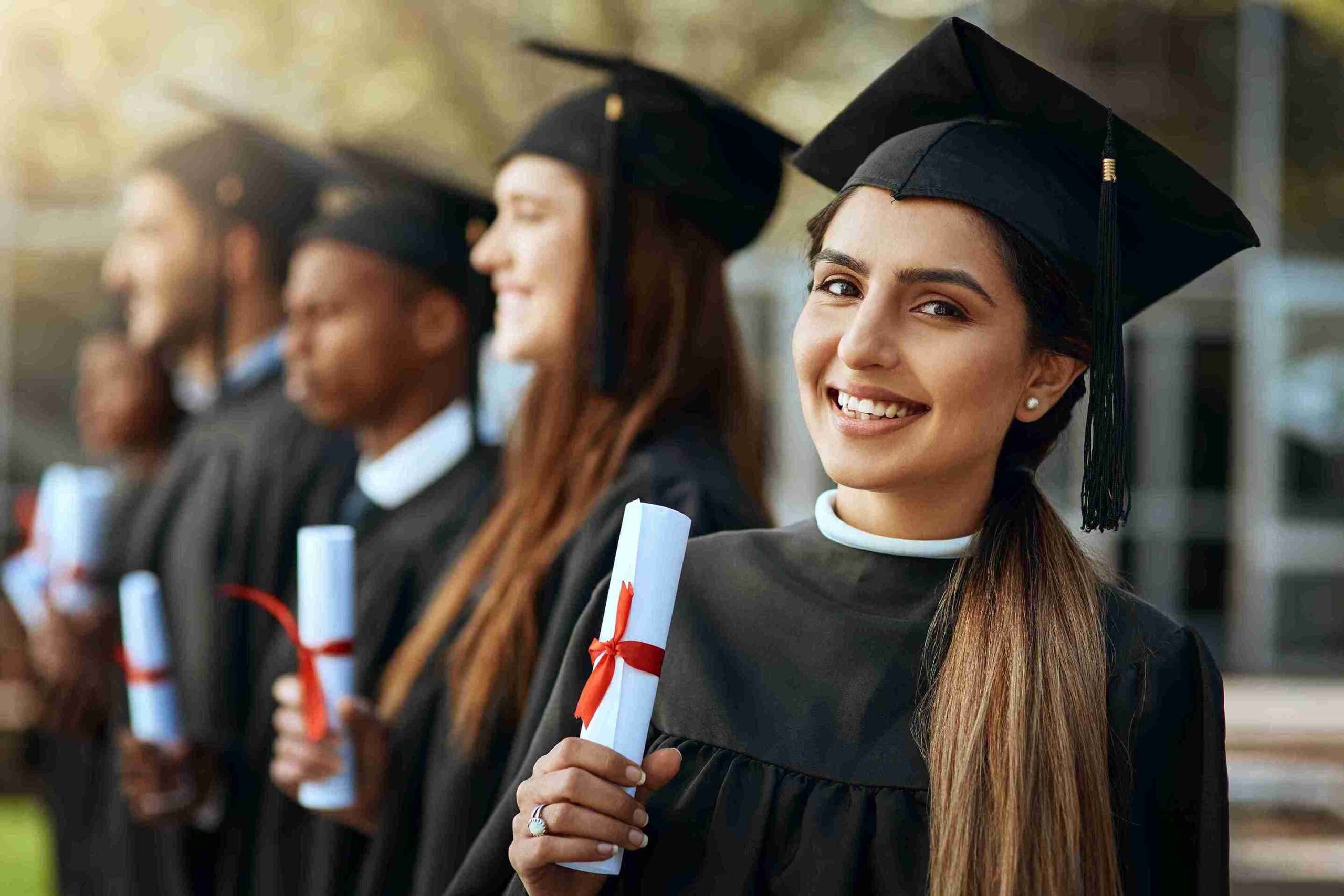 A line of graduates in caps and gowns, smiling and celebrating their achievements together.