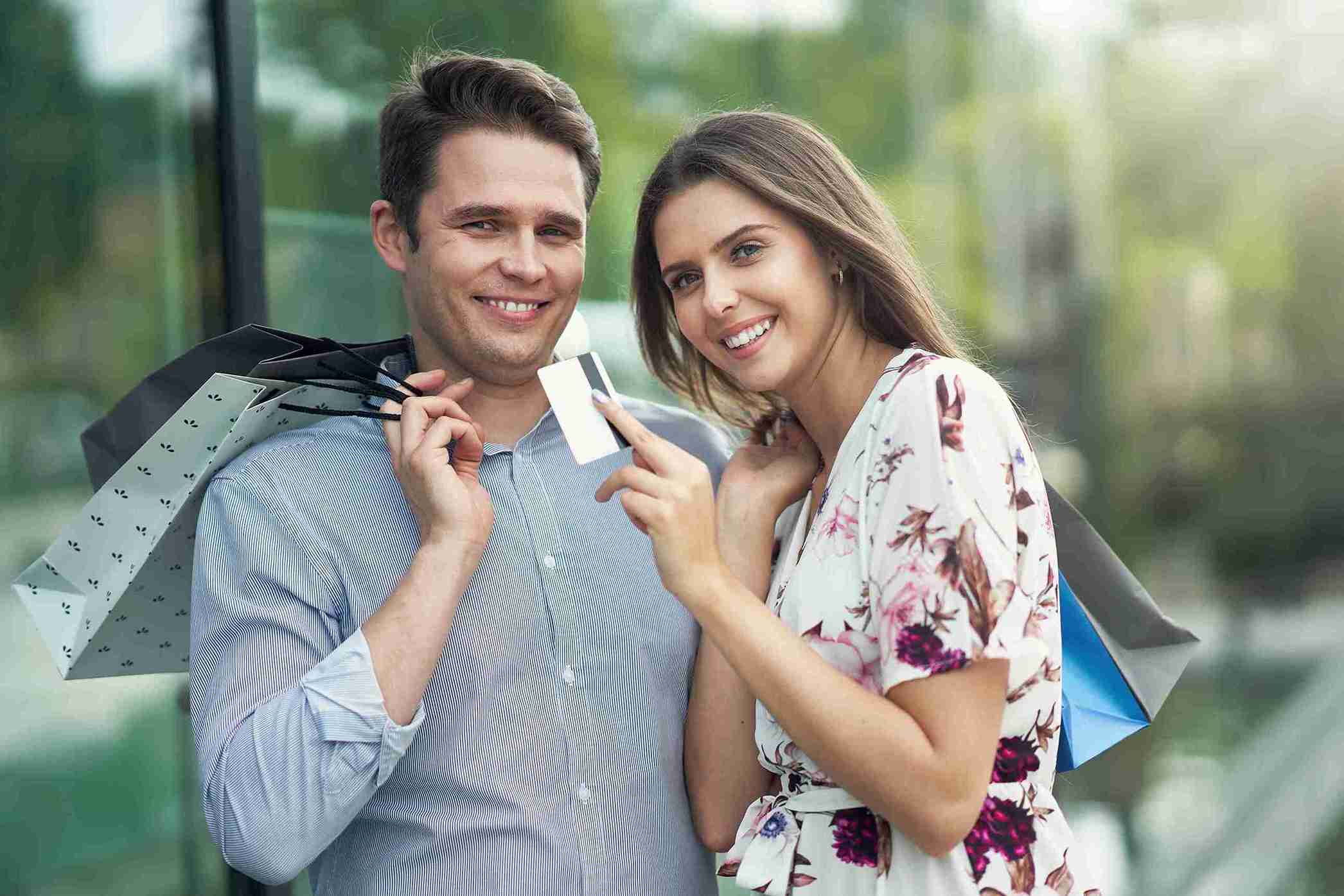 A man and woman smile while holding shopping bags and examining a credit card together.