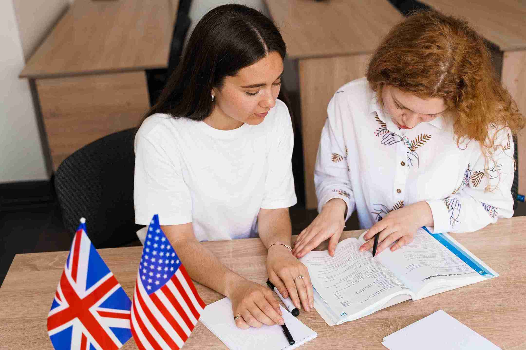Two women sitting at a desk, Study, with an UK flag displayed prominently in the background.