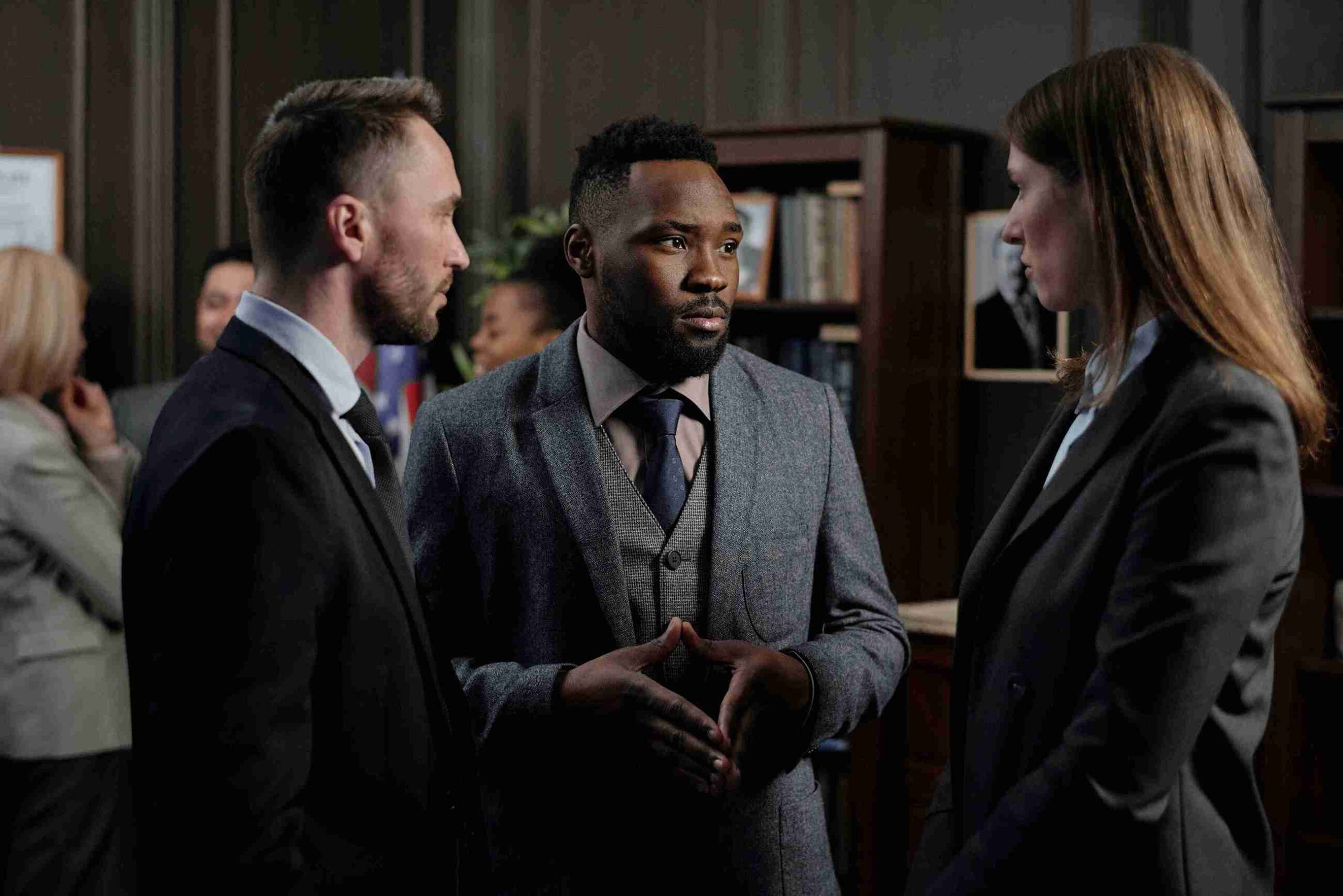 Three professionals in suits engaged in a conversation, sharing ideas in a business setting.