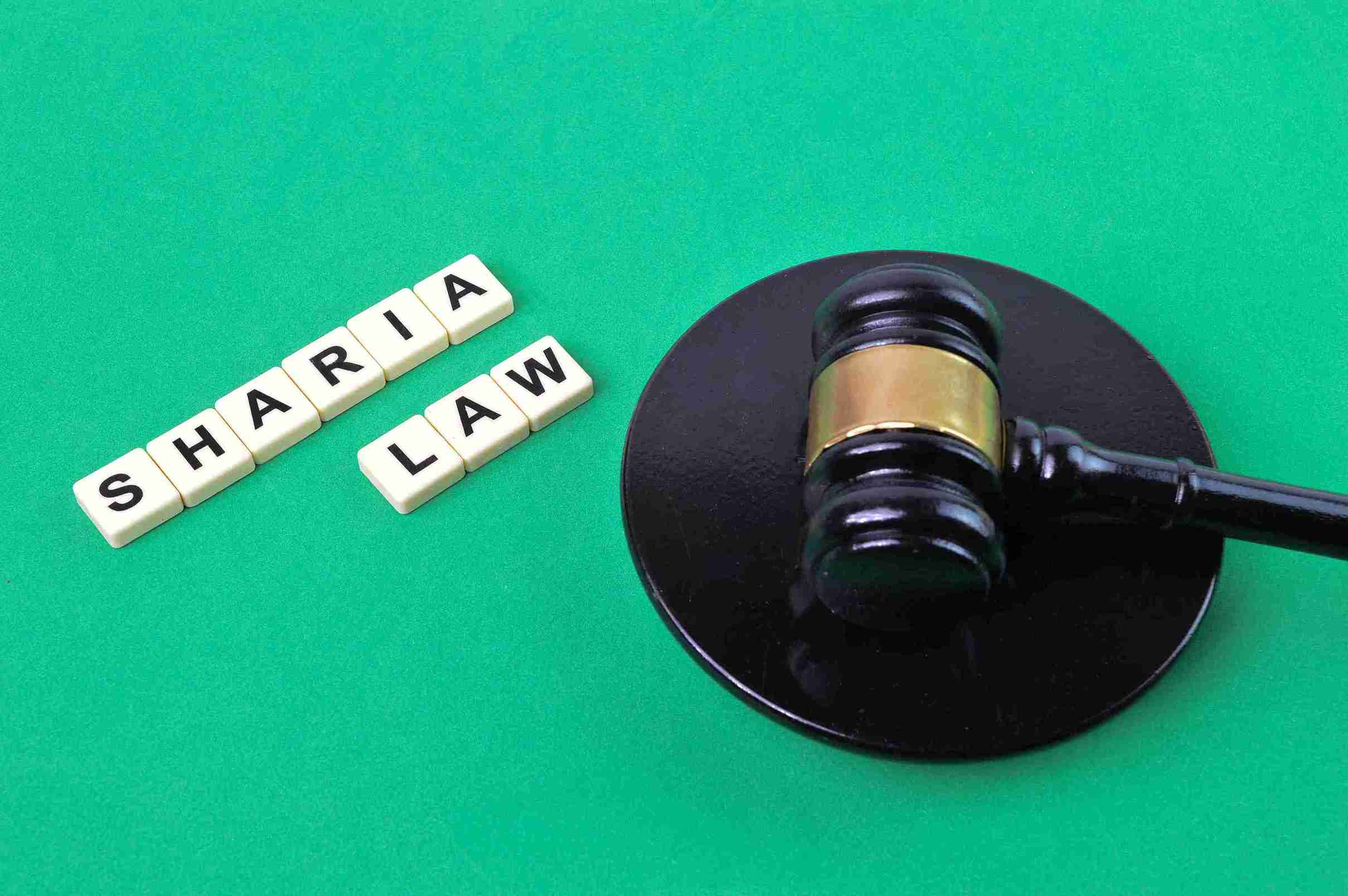 A judge's gavel rests on a circular block against a green background. To the left, tiles spell out "Sharia Law," suggesting a legal concept theme.