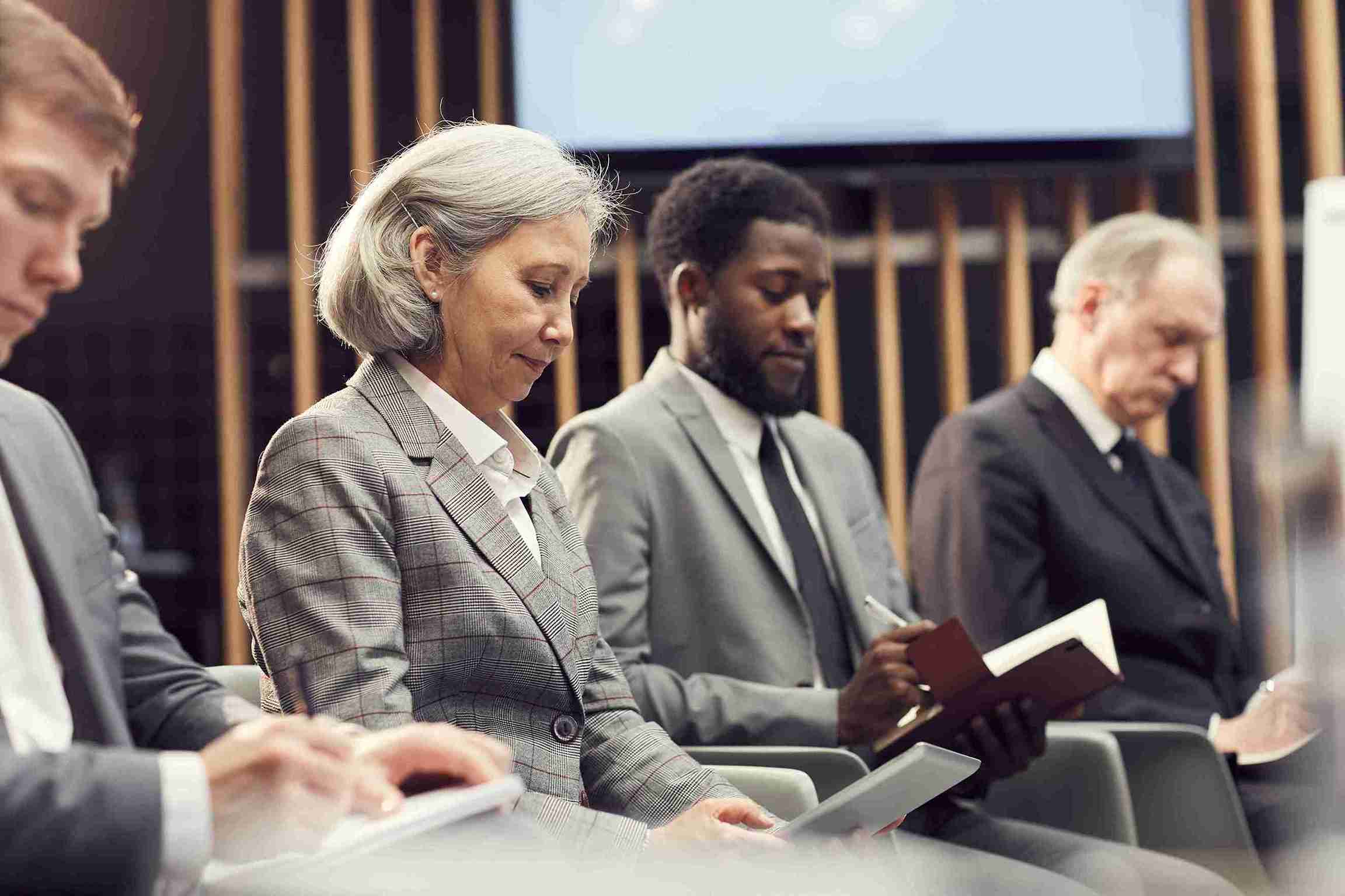 A group of people sitting in a row, focused on summarizing information during a meeting.