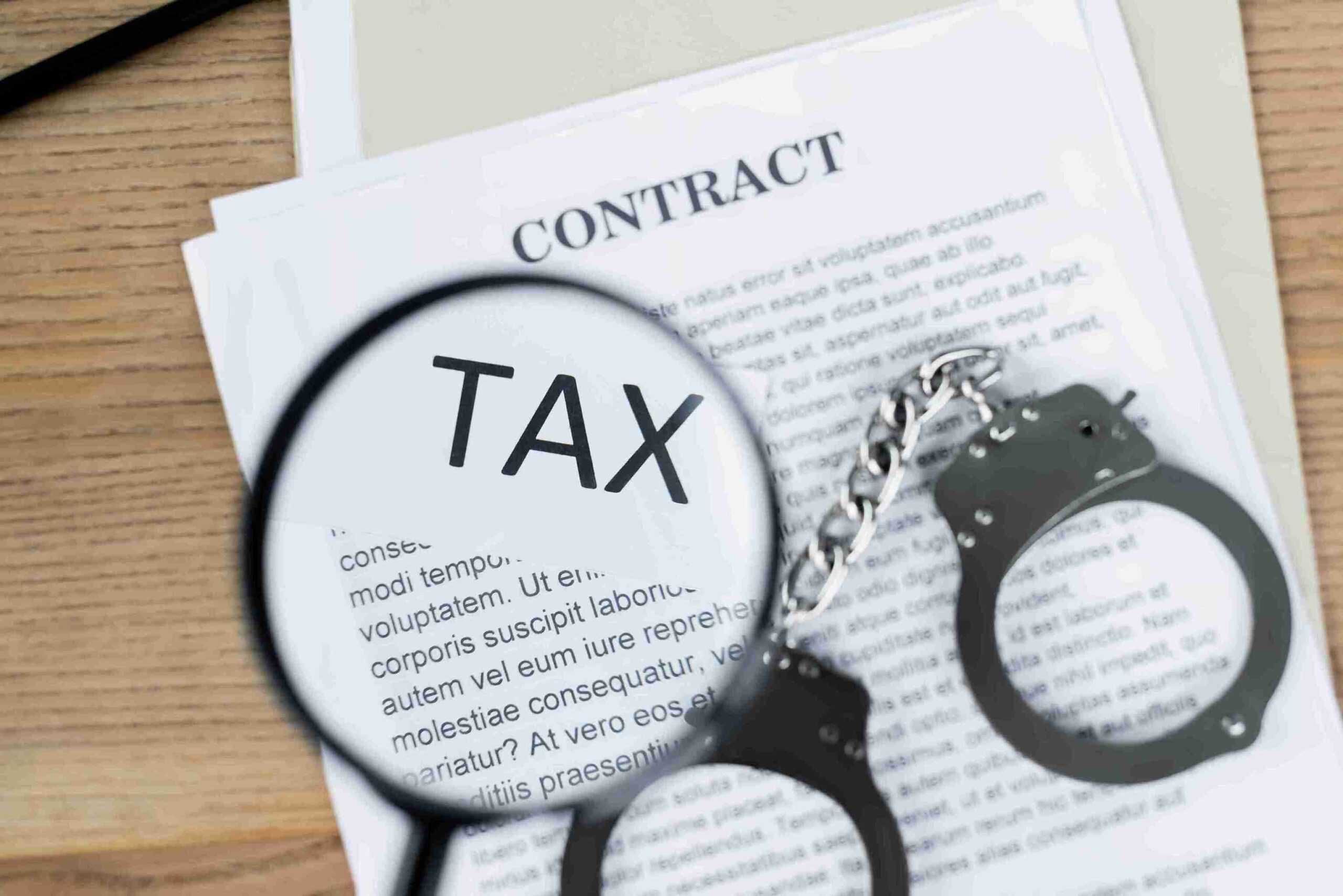 Tax contract with handcuffs and a magnifying glass, symbolizing scrutiny and legal consequences in financial matters.