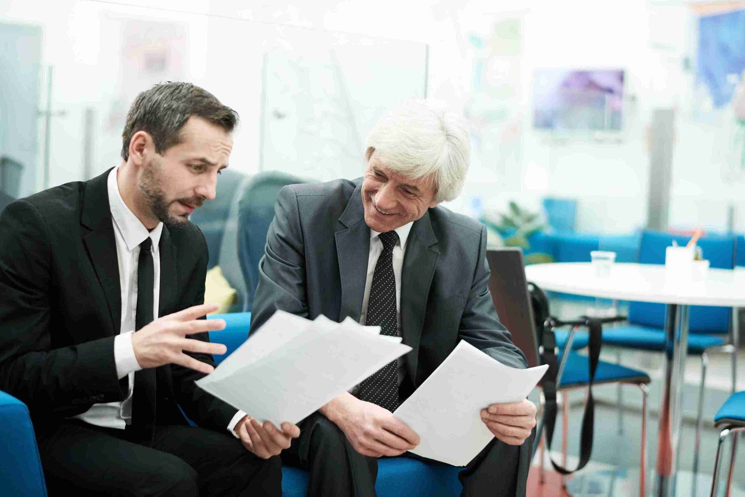 Two men in suits sit on blue chairs, reviewing documents related to the Sole Representative Visa.