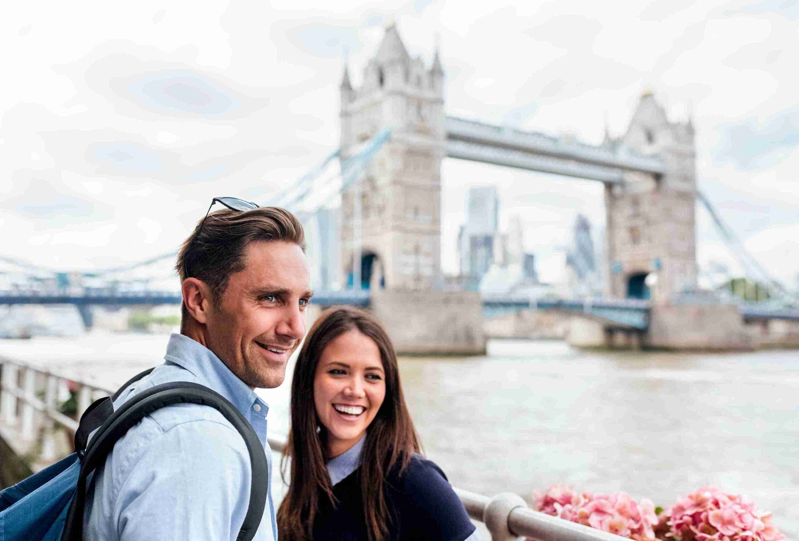 A smiling couple poses in front of Tower Bridge, celebrating their visit to the UK on a tourist visa.