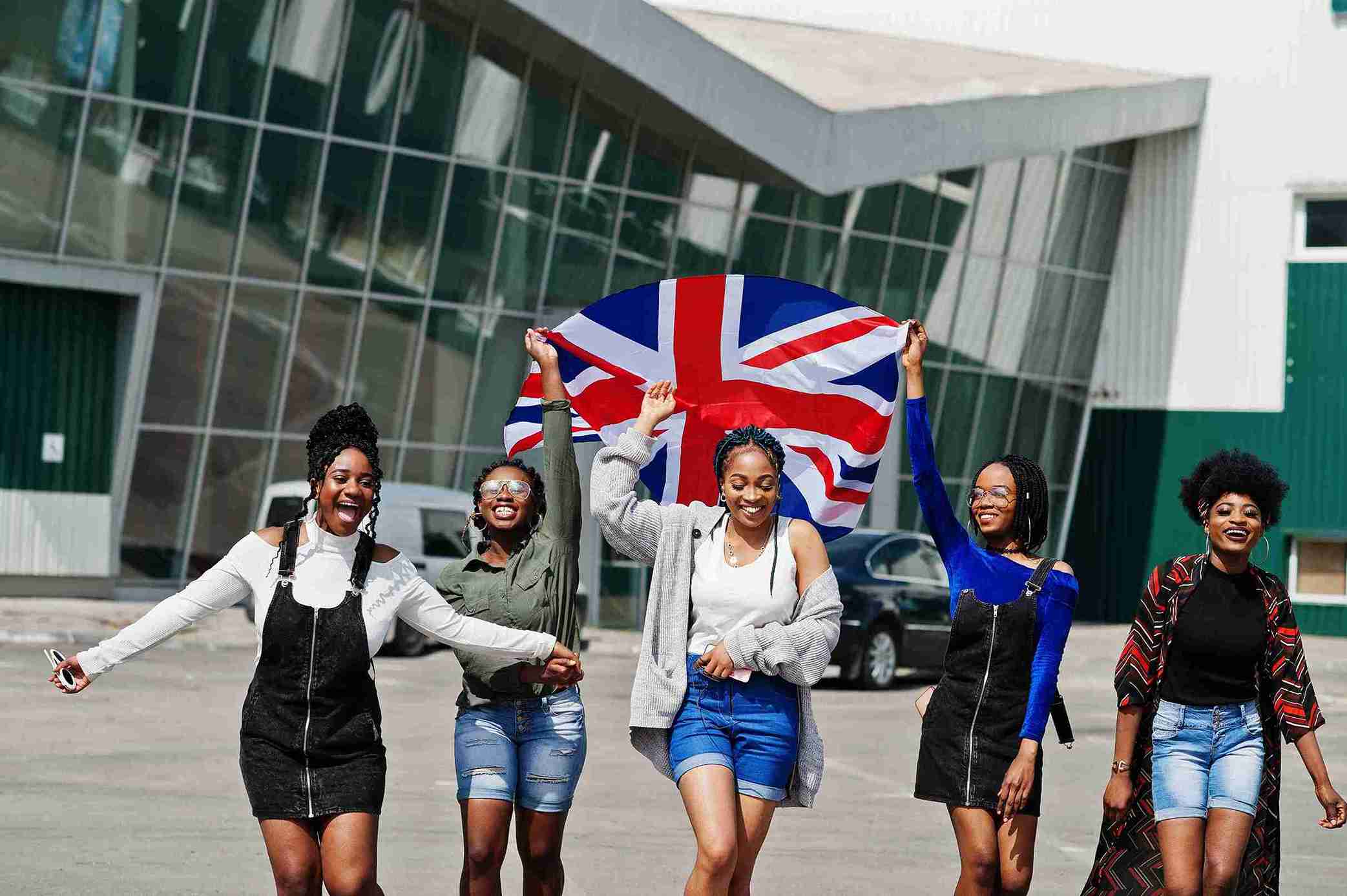 A group of young women joyfully holding up a British flag, celebrating the UK Global Talent Visa opportunity.