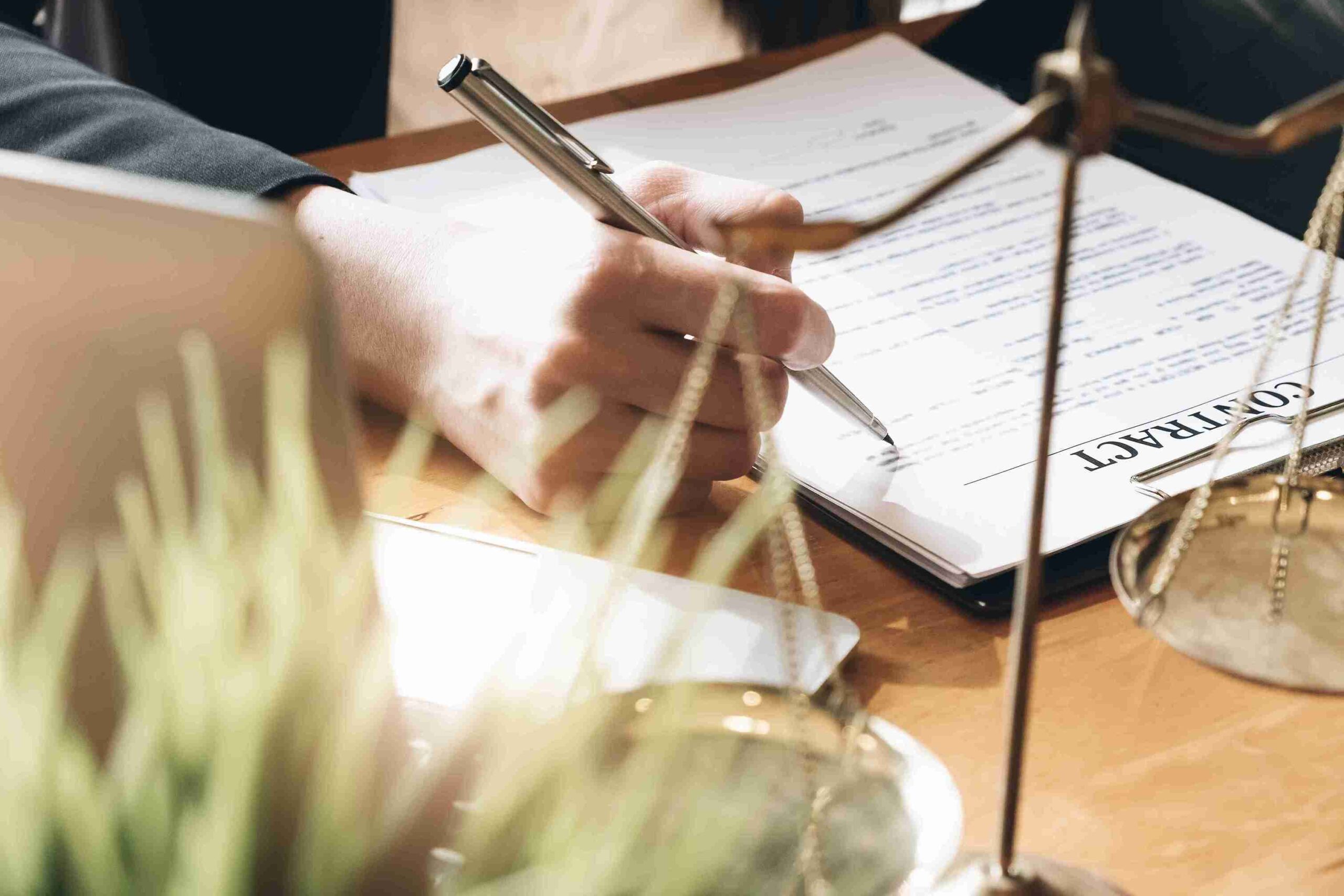 Person signing a contract at a desk with scales of justice, representing personalised legal expertise with transparency and professionalism.