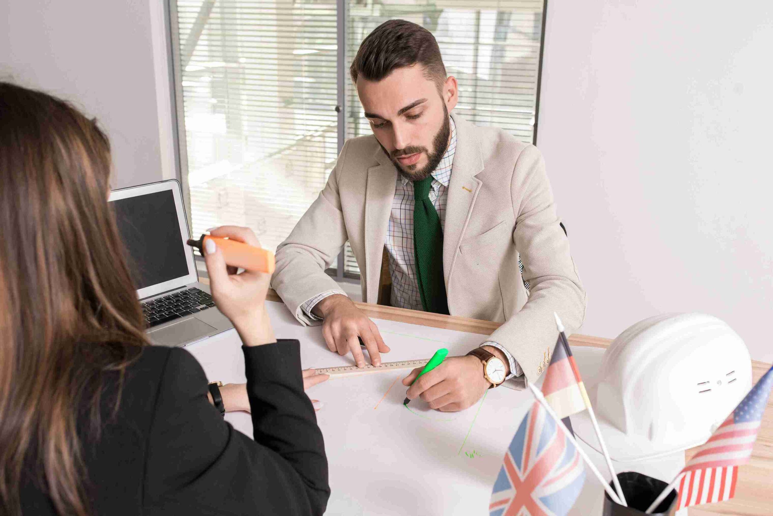 A man and woman in business attire collaborate at a desk, focused on their work and engaged in discussion.