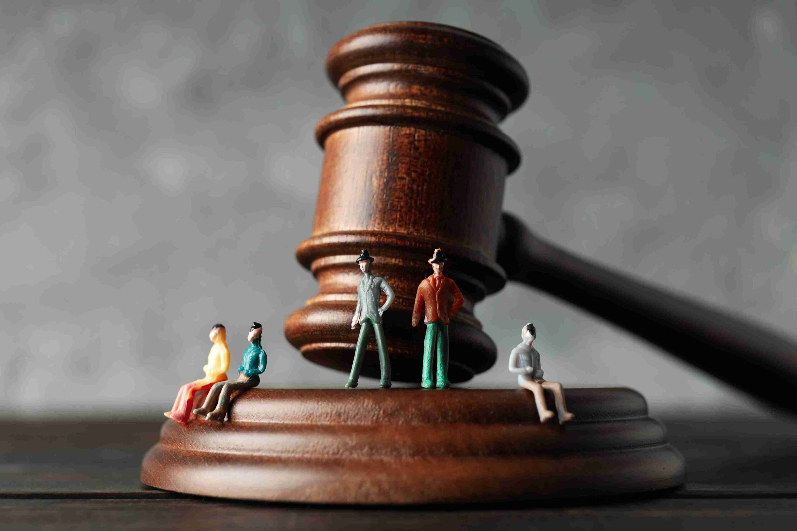 Tiny figurines on wooden gavel, representing regulated professionals facing disciplinary action, suspension, or reputational risks.