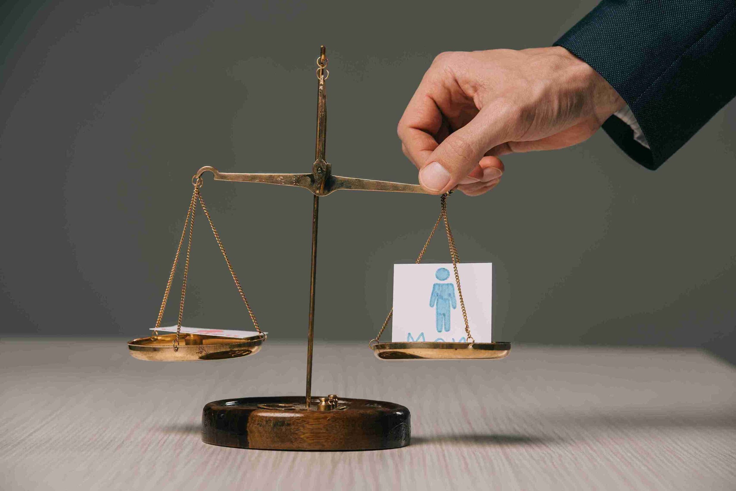 Hand adjusting balance scale with male and female symbols, representing employment tribunals resolving disputes with financial and reputational.