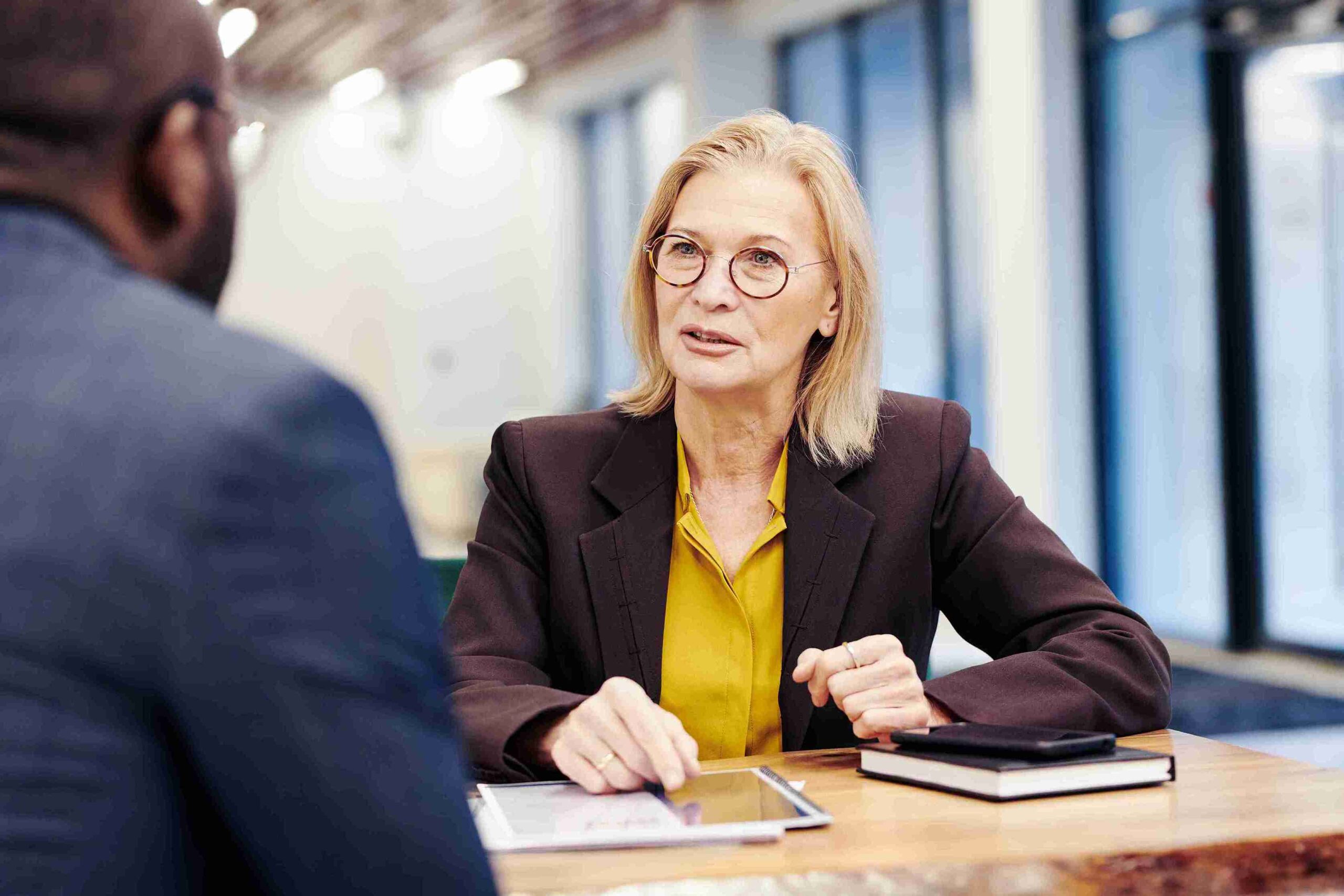 Elderly woman in professional attire consulting with a man at a desk, representing solicitors providing confident guidance to start the process.