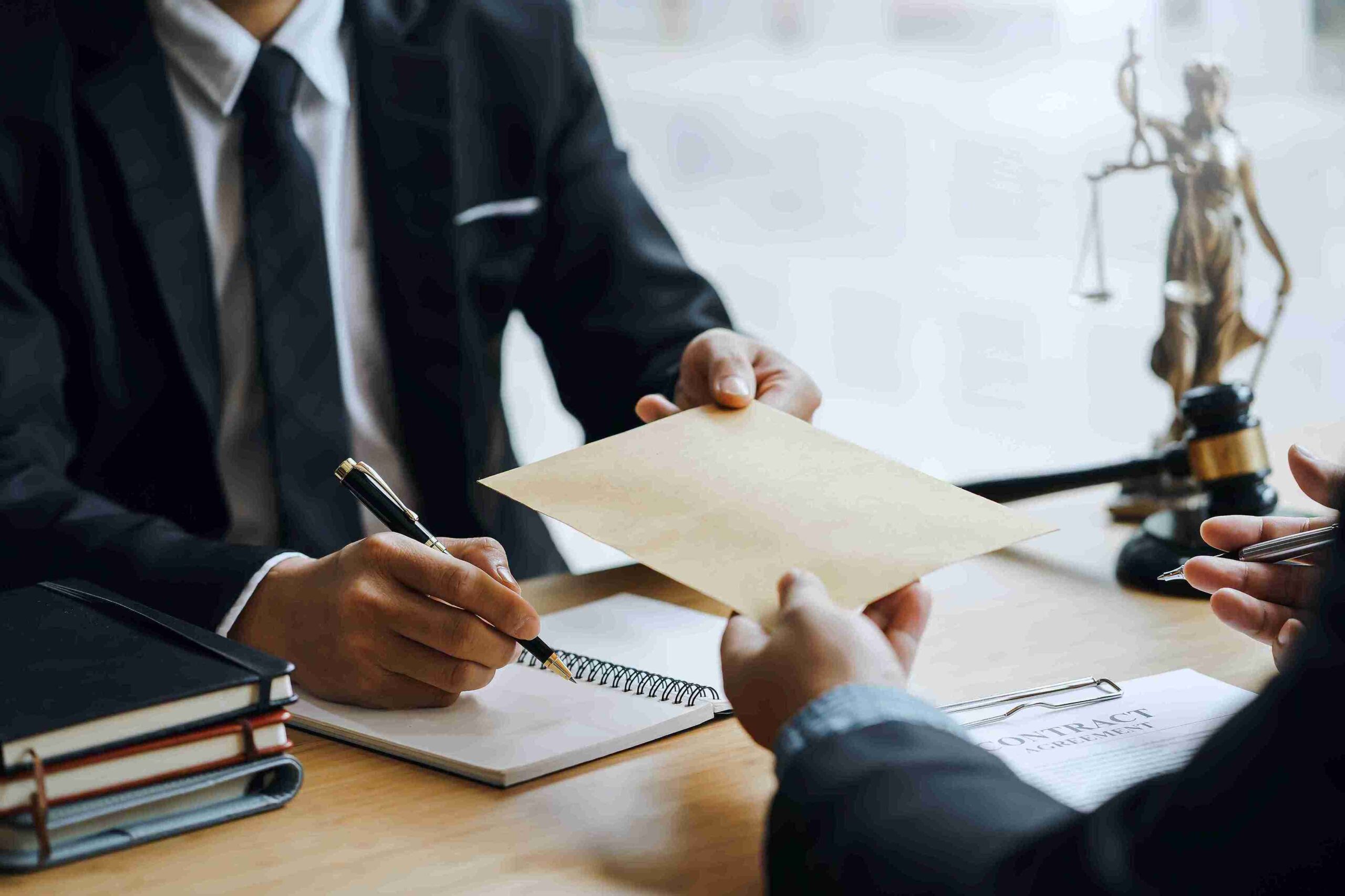 Two people in suits are seated at a table during a meeting. One hands an envelope to the other, representing solicitors guiding clients through action steps and legal delivery.