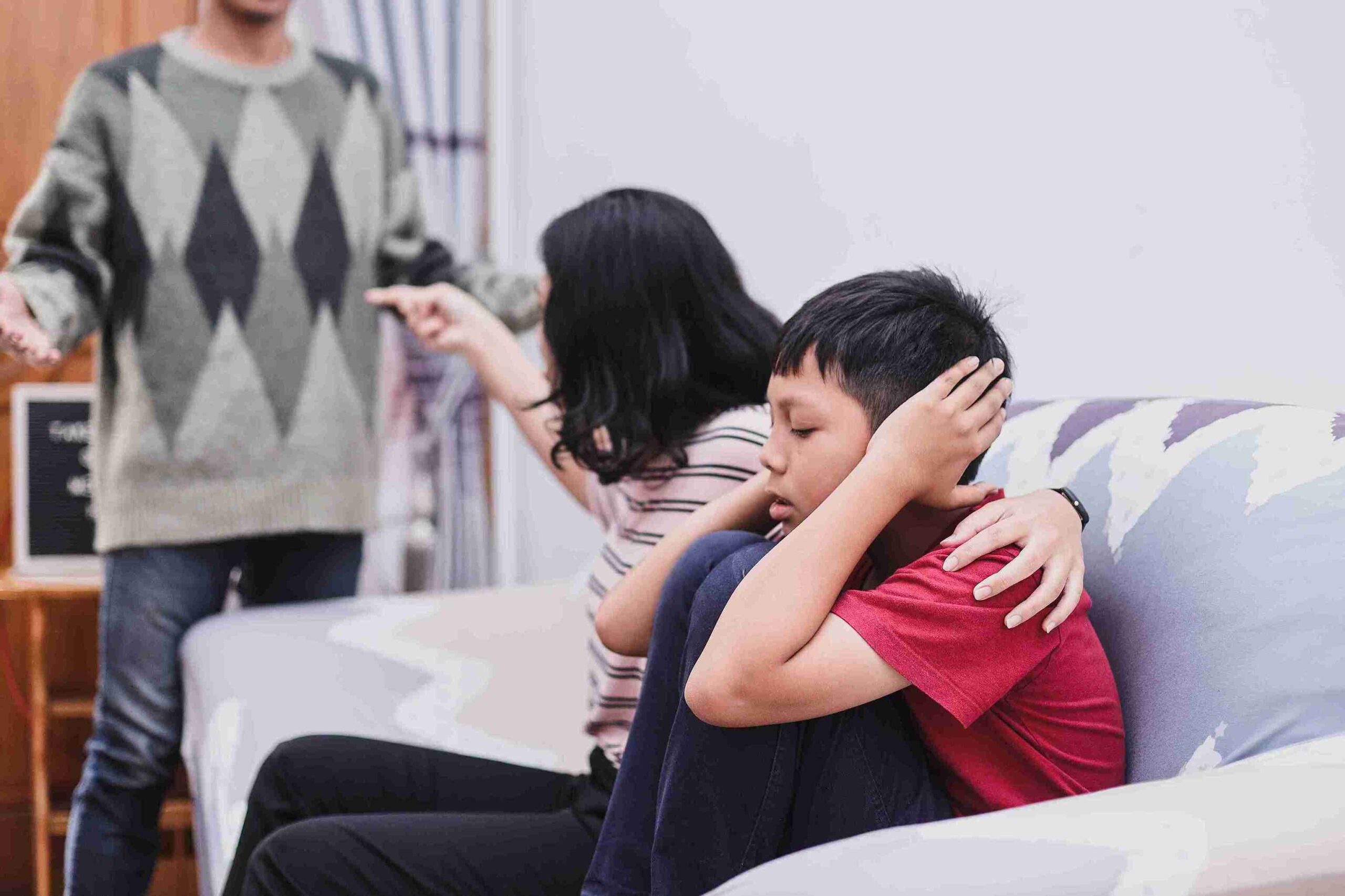 A man and woman are seated on a couch, sharing a joyful moment with a child nestled comfortably between them.