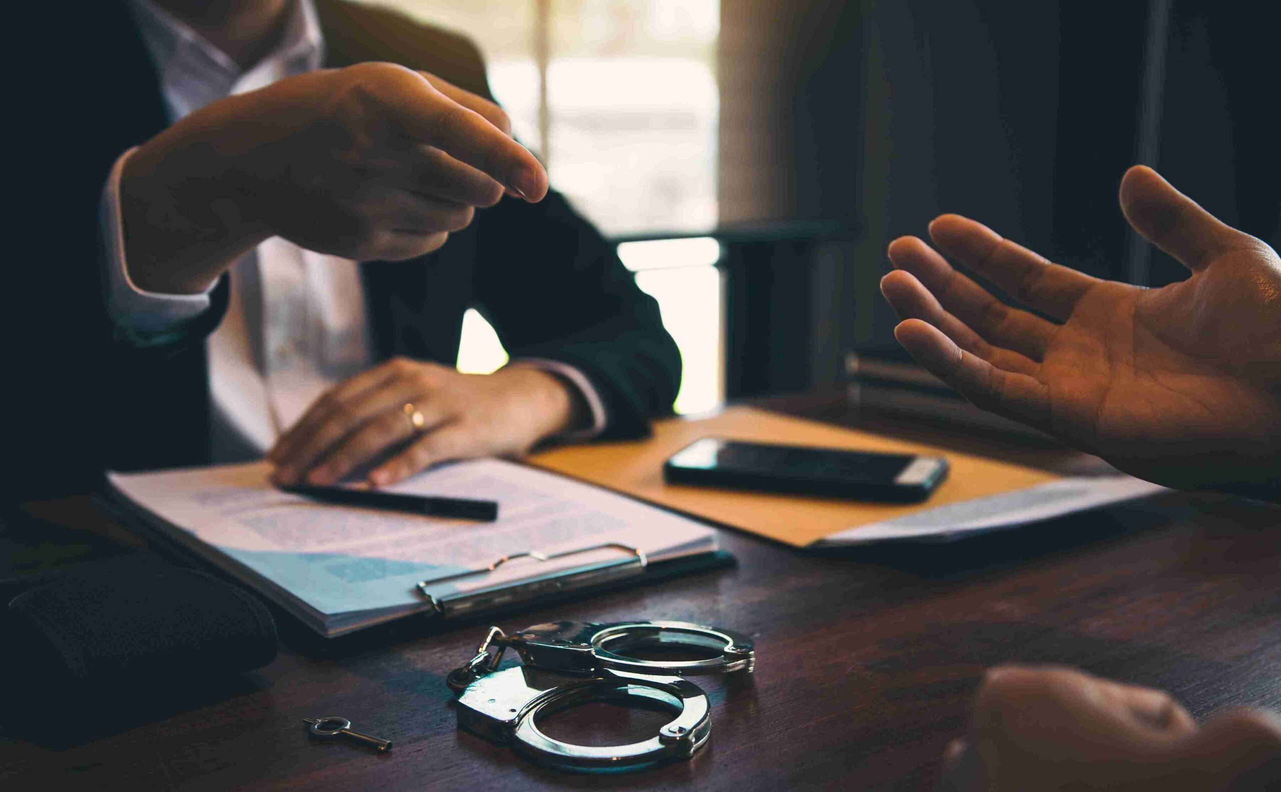 A man investigate to the another man with handcuffs on table, representing expert legal complex inquiries in tax-related fraud investigation.